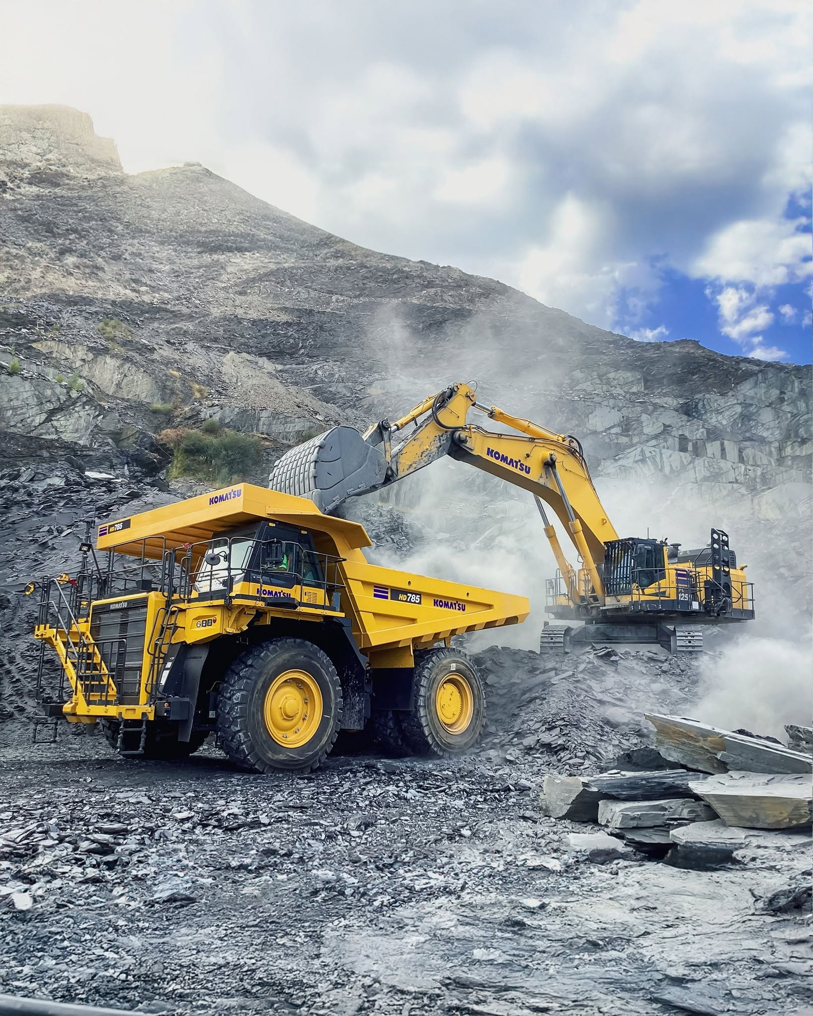 Excavator besar memuat dump truck di area tambang terbuka